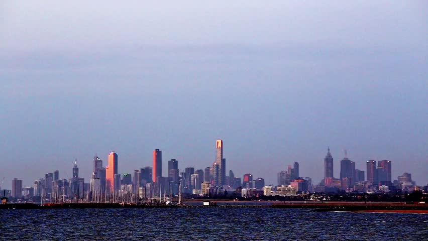 Establishing shot of Melbourne, Victoria, Australia skyline in the late afternoon, looking across water, with pink sunset reflection on buildings. Viewed across the water of Port Phillip Bay.