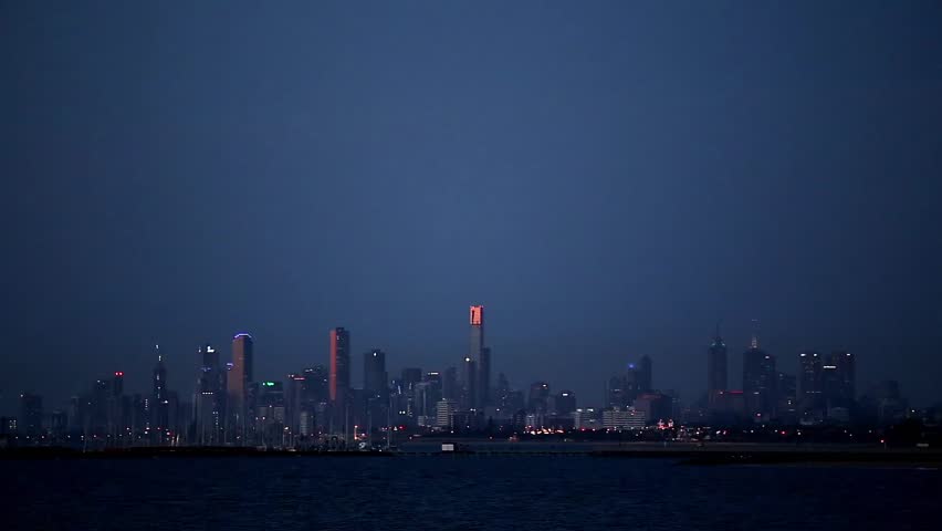 Establishing shot of Melbourne, Victoria, Australia skyline at night with lights twinkling on buildings and traffic. Viewed across the water of Port Phillip Bay.