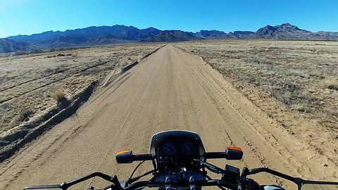 Time lapse shot of the viewpoint of a motorcycle rider speeding on a dirt road in the desert. The handlebars can be seen here bouncing around over the rough terrain in fast motion.