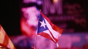 Evening shot of two Puerto Rican flags being held outdoors at an event. SInce it is a close-up, aside from the flags only the hands of the people can be seen but no faces.