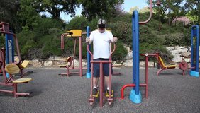 A big man with 3D VR head mounted display in outdoor gym. The athlete watches a movie while getting an exercise. 