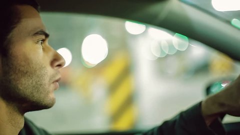 A man driving the car at undergroung parking. Close up. Bokeh background