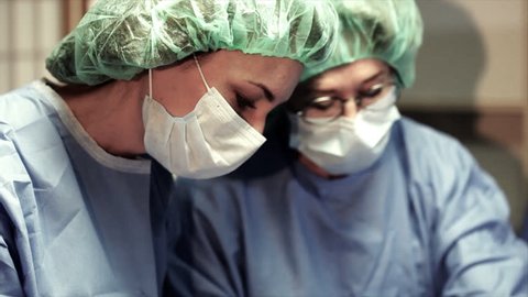 The camera tilts and pans revealing three surgeons engaged in a surgical procedure in an operating room.