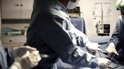 A surgical nurse hands a surgeon a hypodermic needle during surgery.