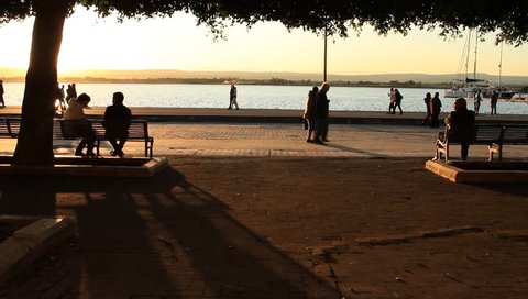 Sicily, Siracusa_Jan. 2012: One couple and one man sitting on bench overlooking ocean in Sicily, Italy