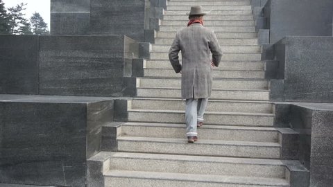 Climbing the stairs to the monument of man with the hat, red scarf and coat close up shot aerial