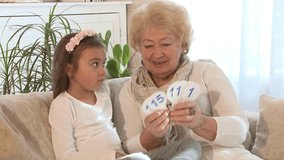 Grandmother showing numbers with her granddaughter, while they are sitting on the sofa in the living room
