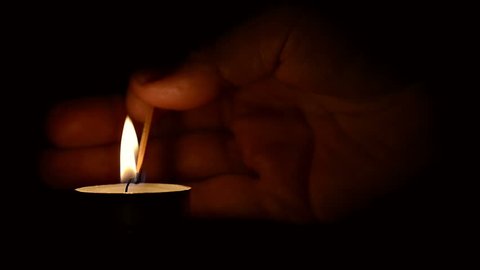 Hand lighting a candle with a match at night with a black background