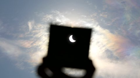 Partial sun eclipse on blue sky background. Man covering strong sunlight by dark plastic plate and showing partial sun eclipse.