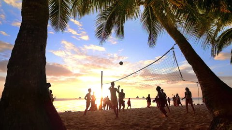 Slow motion. Sunset silhouette of people playing volleyball at tropical beach under palm trees. Boracay island, Philippines summer vacation
