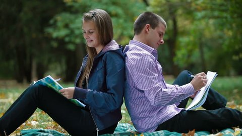 Two students studying in autumn park writes something in notebooks