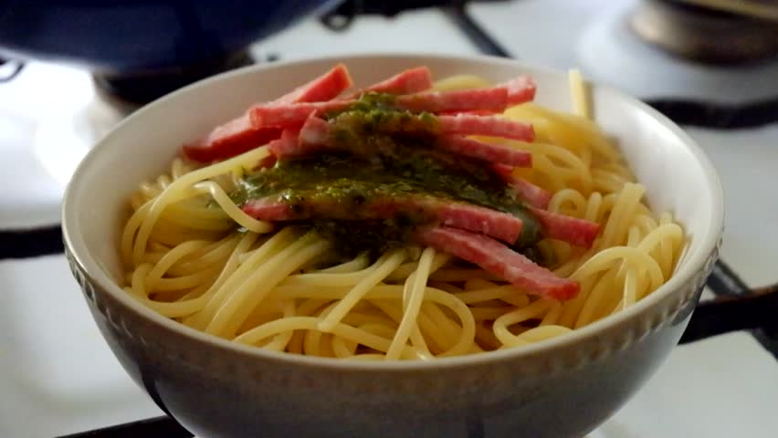 Putting green pesto sauce on spaghetti .