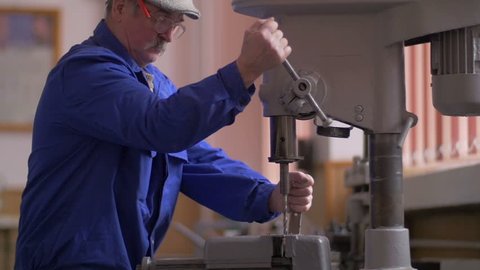 Man drilling with a machine making a hole in a steel bar