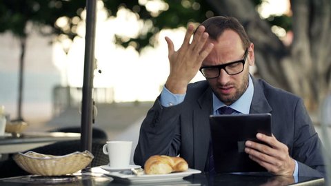 Unhappy businessman with smartphone and tablet computer reading bad news in cafe
