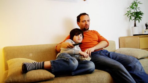 Father and son wathing tv and eating popcorn: stockvideo