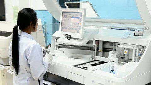 Woman working in the modern medical laboratory. Medical staff working with automatic machine. Analysis blood at hospital laboratory. Doctor testing blood samples in a robotic machine with display.