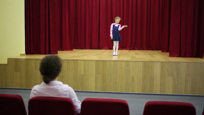 Back of woman looking on performing girl on stage. Focus on girl