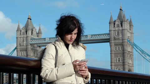 London, tourist using smartphone with London tower bridge in background