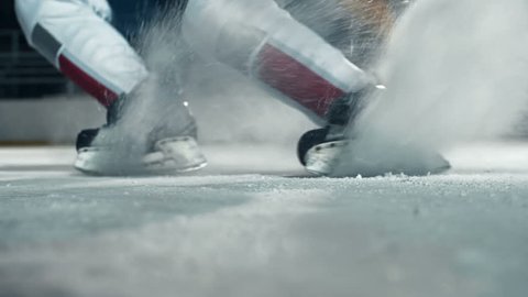 Low angle of hockey player running towards camera on skates and doing a turn cutting ice to powder
