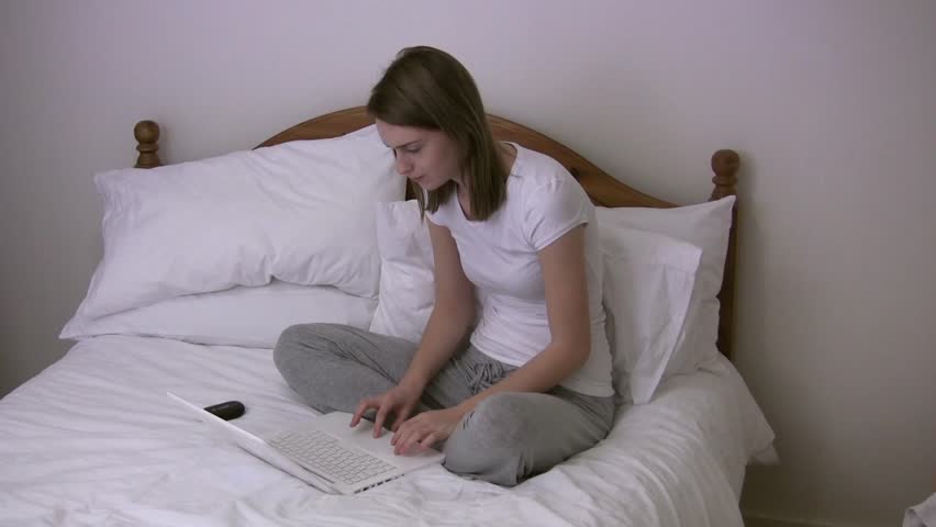 Young woman aged 20-25 at home, sitting on double bed, typing on laptop, and using cell phone Royalty-Free Stock Footage #9355205