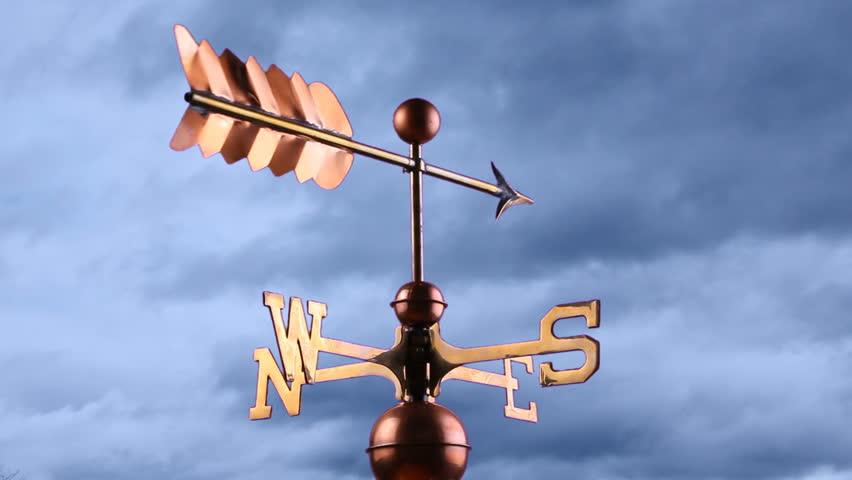 A moving weather vane against a dark cloudy sky
