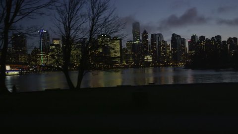 Dolly shot of Vancouver skyline at night in January, with runners in silhouette along the seawall in foreground.
