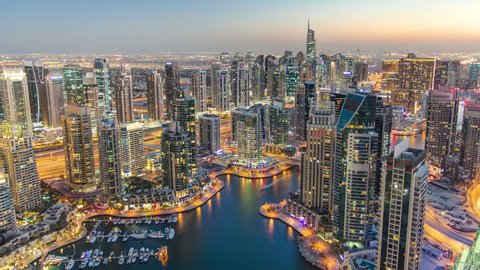 Dubai Marina with yachts in harbor and modern towers from top of skyscraper transition from day to night timelapse, Glittering lights and tallest skyscrapers during a clear evening with Blue sky. 4K