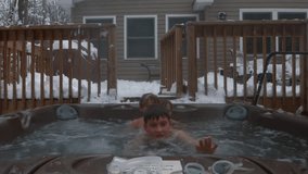 Three young boys play together and swim in a hot tub in the backyard of their home.