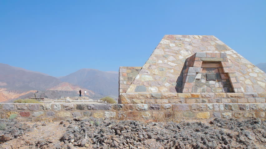 Archaeological site "Pucara de Tilcara" at the Humahuaca valley in north-west Argentina. Pyramid monument in the foregr. Two persons talk in the backgr. A few grass stalks move slightly (1080p).
