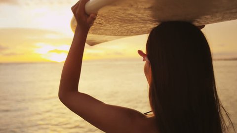 Young female surfer going surfing holding surfboard at sunset. Beautiful ethnic mixed race Asian Chinese / Caucacsian woman sport model. Sun flare and colorful silhouette. Waikiki, Oahu, Hawaii, USA. Stock video