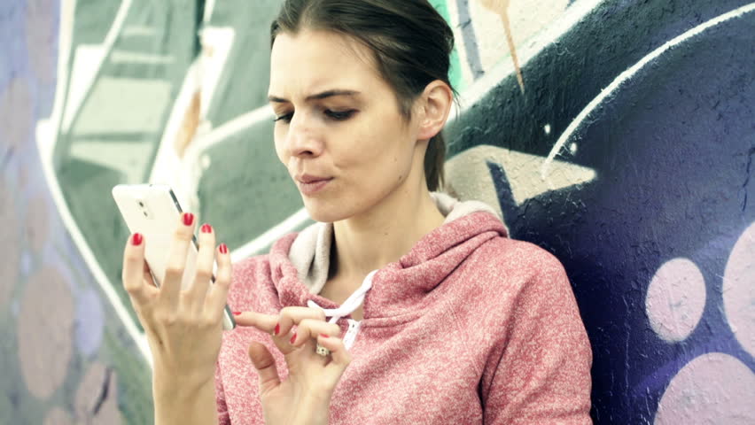 Young, happy woman talking selfie photo with cellphone standing by the graffiti wall
