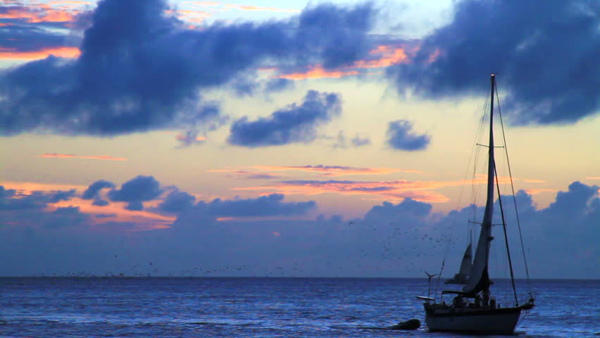 small sailboat slowly makes its way along the setting sun