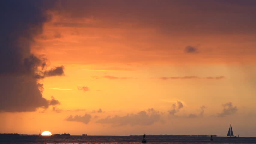 small sailboat slowly makes its way across the sea as the sun sets