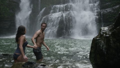 Wide panning slow motion view of couple in swimming hole near waterfall: Santa Juana, Costa Rica