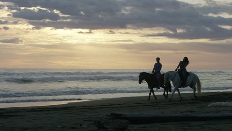 Wide panning shot of couple riding horseback on beach: Esterillos, Puntarenas, Costa Rica