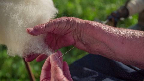 Spinning the wool to make a string. Slow motion close up RAW footage of a woman seating on a bench and spinning the wool to make a string on traditional way.