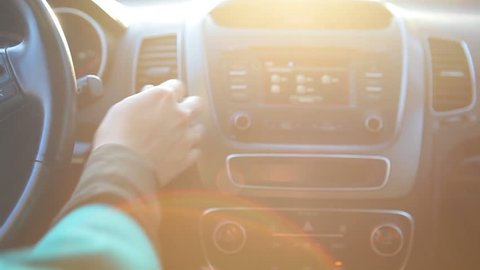 Woman hand turning on radio on car dashboard in sunny day