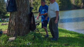 Fishermen weighing just caught a fish. Slow motion RAW footage of a two man standing next to the tree and weighing just caught fish close to the lake.