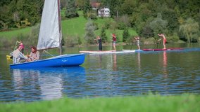 Couple enjoining on the boat sailing on a lake. Slow motion RAW footage of a boat sailing on the lake and surfers paddling in the beck ground on a sunny day.