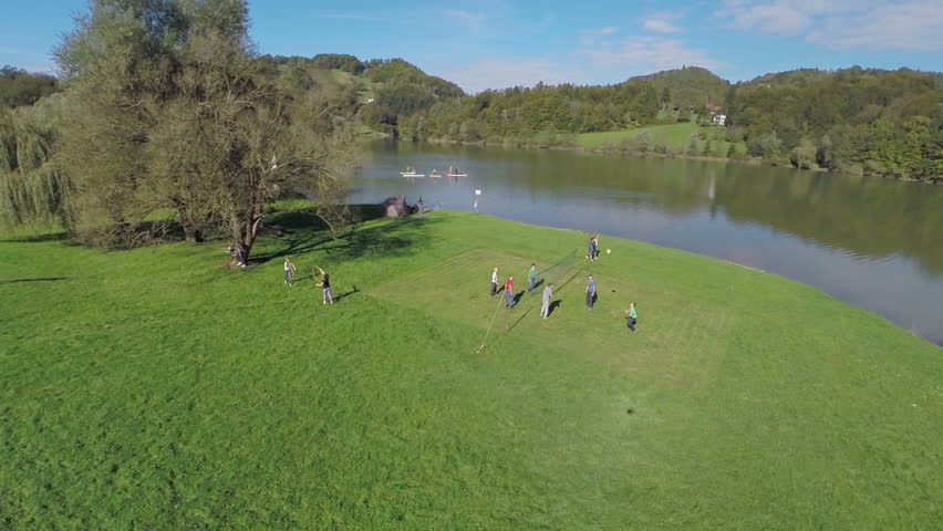 People outdoor on the sunny day. Slow motion helicopter camera flaying over the lake and capturing kids playing on the lawn close to the lake.