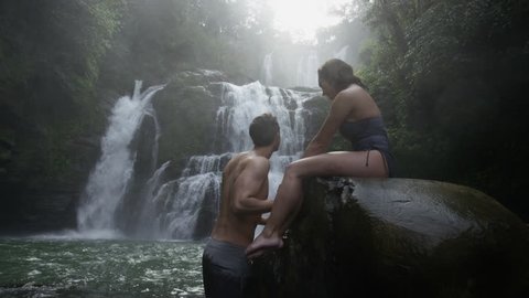 Wide panning slow motion view of couple swimming near waterfall: Santa Juana, Costa Rica
