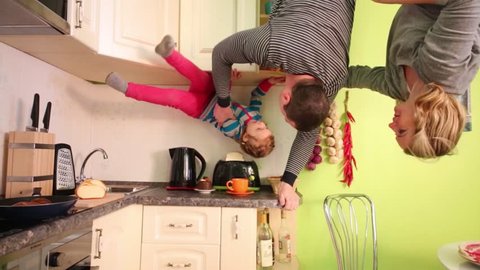 Parents and daughter upside down have fun in green kitchen of inverted house