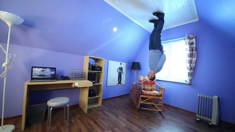 Young man in jeans stands upside down in inverted house at sunny day