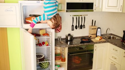 Little girl upside down looks into fridge in small kitchen in inverted house