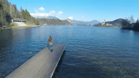 Person walk on lake pier aerial fly around 4K. Beautiful landscape view from wooden pier, female woman walking to the edge looking around and turning back. Flying around with quadcopter.