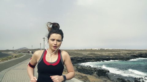 Young woman with smartwatch jogging by sea
