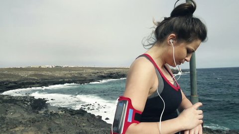 Young female jogger with smartwatch checking pulse by sea
