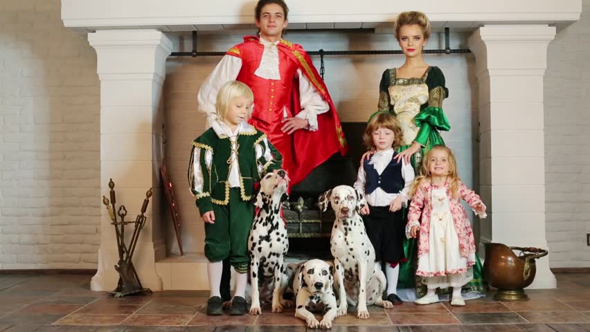 Father, mother in medieval costume with three children and three dalmatians stand near chimney