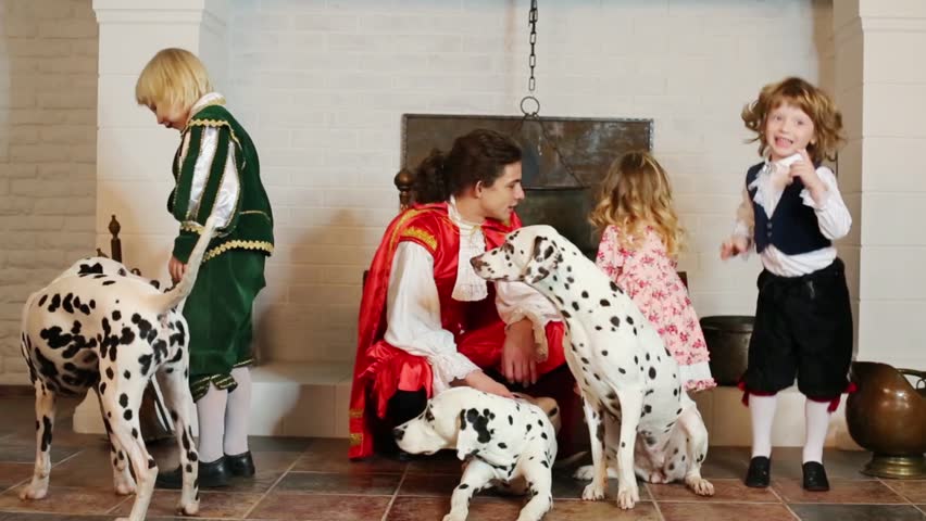 Father in medieval costume with three children and three dalmatians sit near chimney