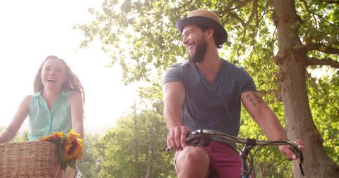Young couple cycling happily together through a sunny park on street in summertime Stockvideó
